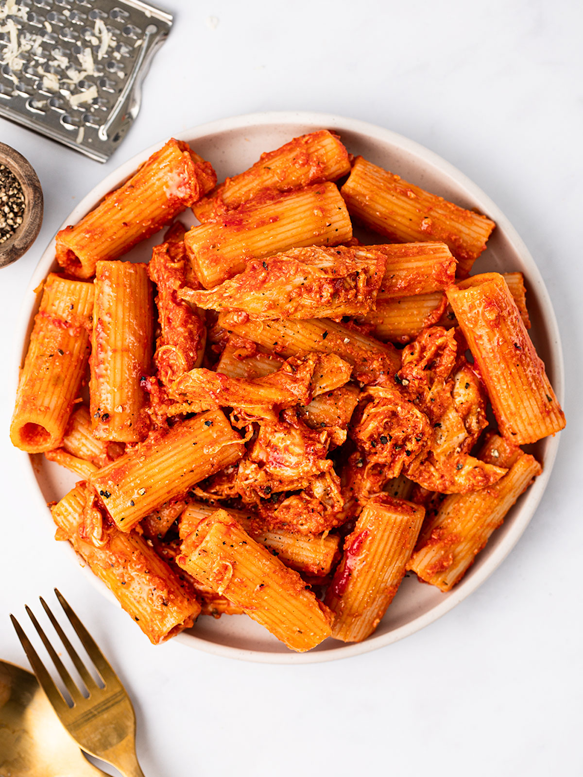 A serving of Cheesy Chicken Pasta in a white bowl with black pepper on the side.