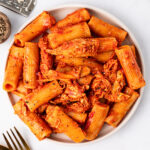 A serving of Cheesy Chicken Pasta in a white bowl with black pepper on the side.