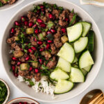 A serving of Ground Lamb Bowl in a white bowl on a white background. With pomegranate seeds and cilantro on the side.