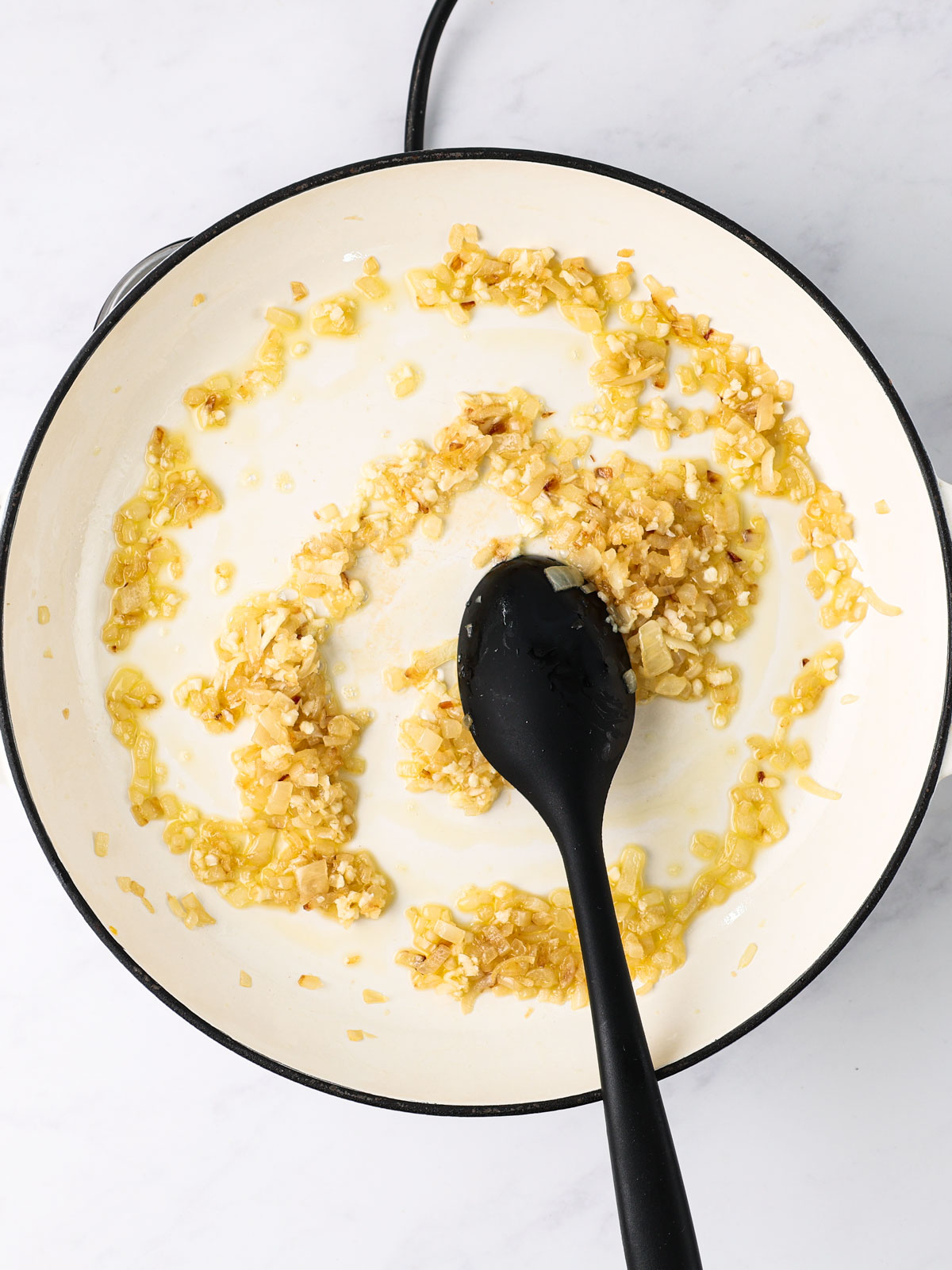 Heating the olive oil in a large skillet over medium-high. Cook onion 3-4 minutes until softened, add garlic for 30 seconds. In a white electric skillet with black spoon on a white background.
