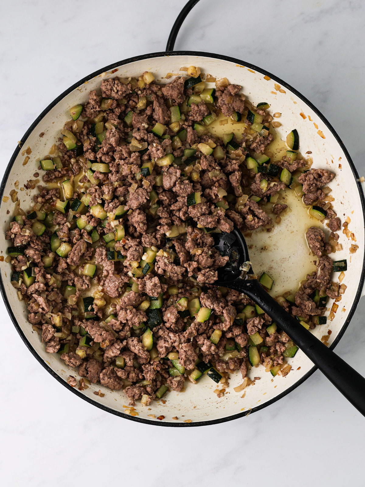 Add lamb, break it up, and cook 5-7 minutes until browned. In a white electric skillet with a black spoon on a white background.