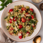 A serving of Pastina Salad in a white brown rimmed bowl with basil, parmesan and black pepper on the side.