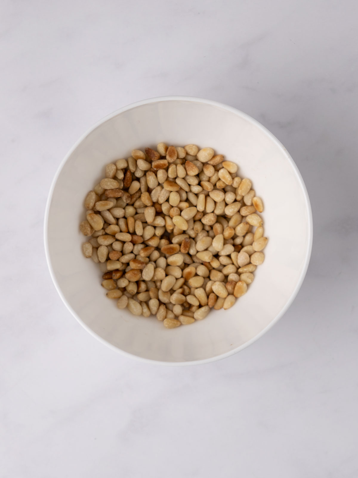 The toasted pine nuts in a white bowl.