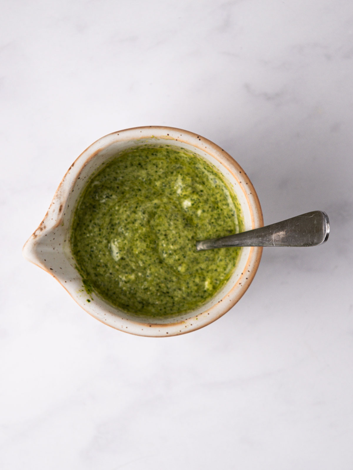 The pesto and mayo whisked together. In a white/brown bowl on a white background.
