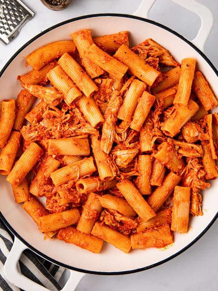 A pan of cooked cheesy chicken pasta on white background.